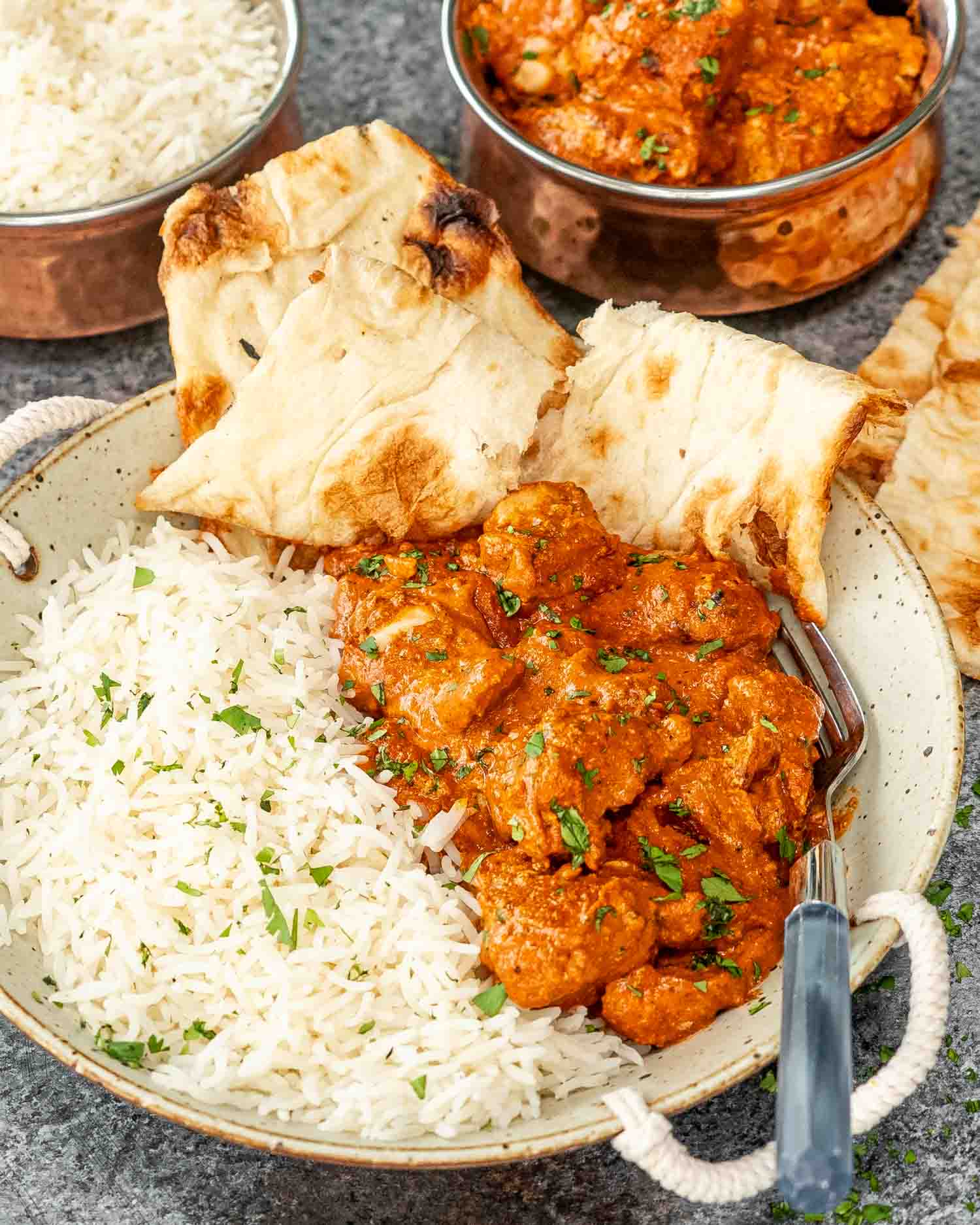 a serving of chicken tikka masala with rice and naan in a plate.