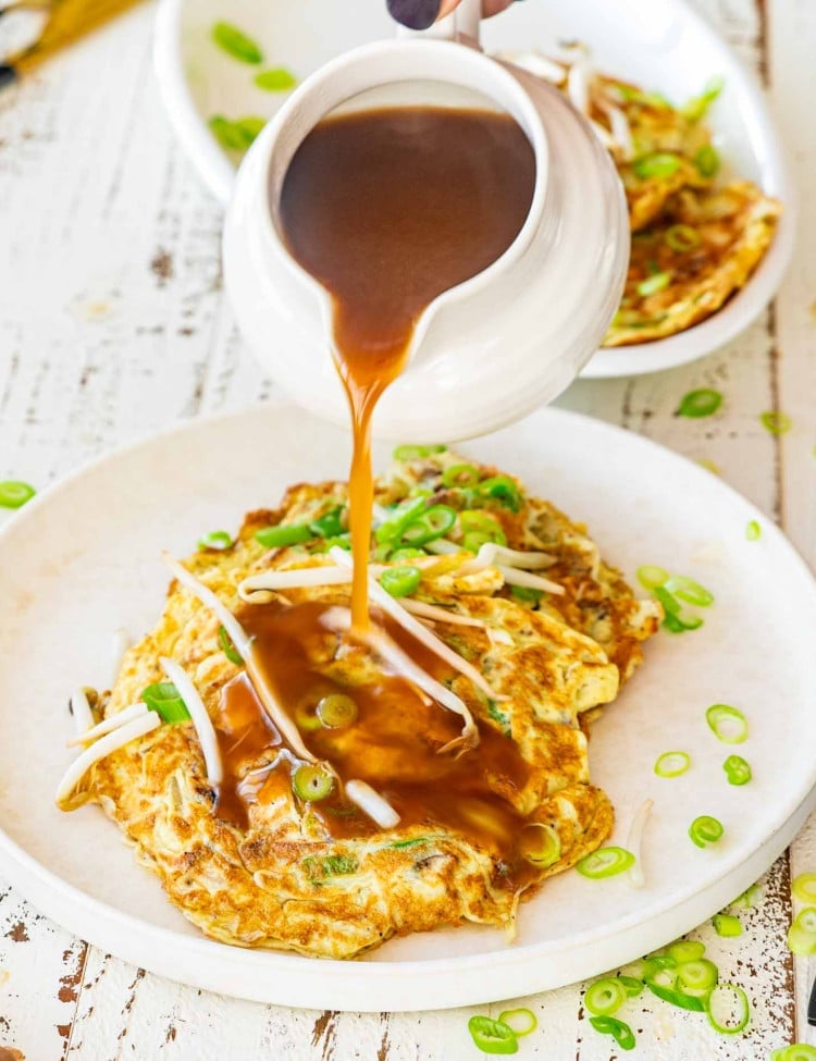pouring sauce on egg foo young on a white plate.