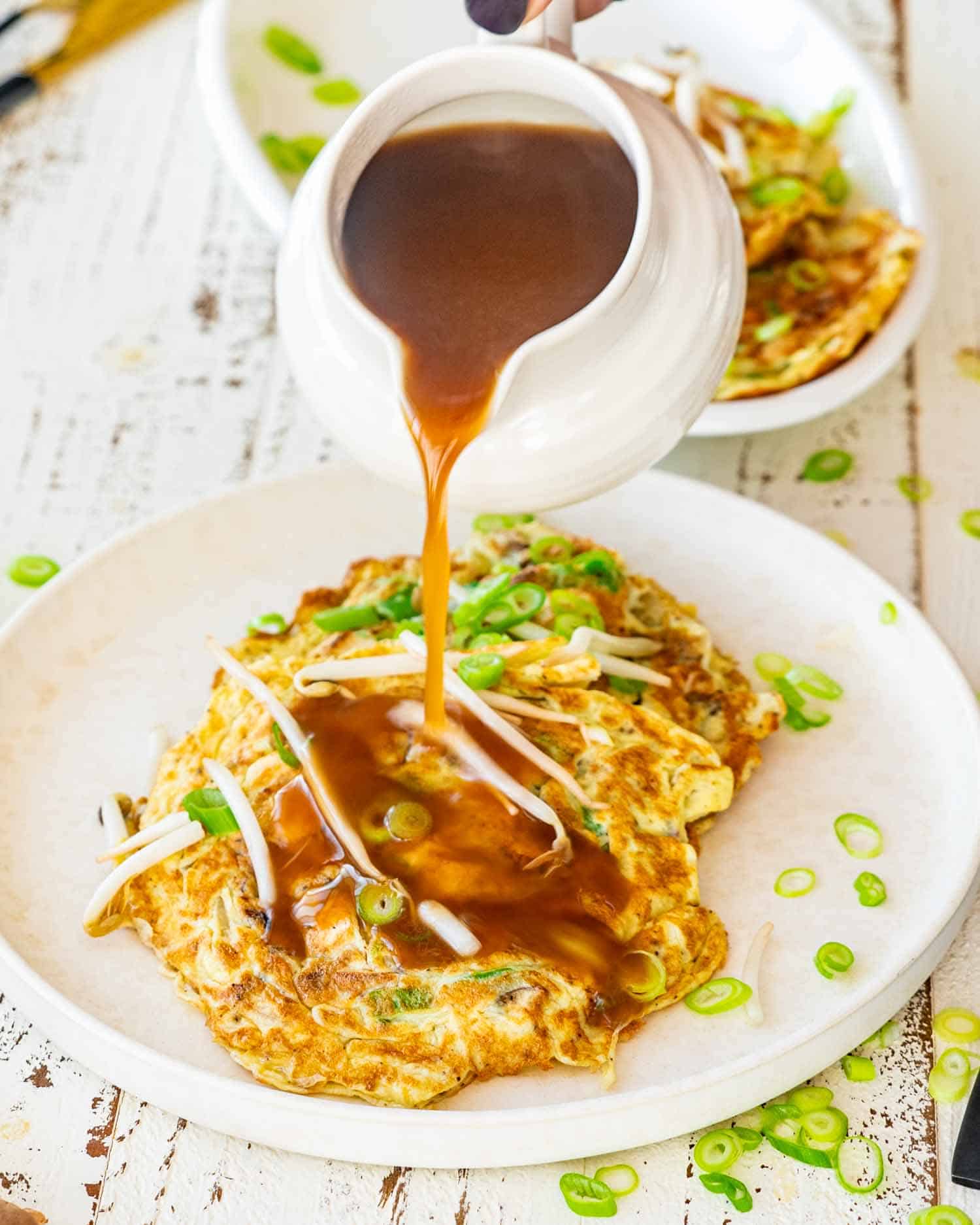 pouring sauce on egg foo young on a white plate.