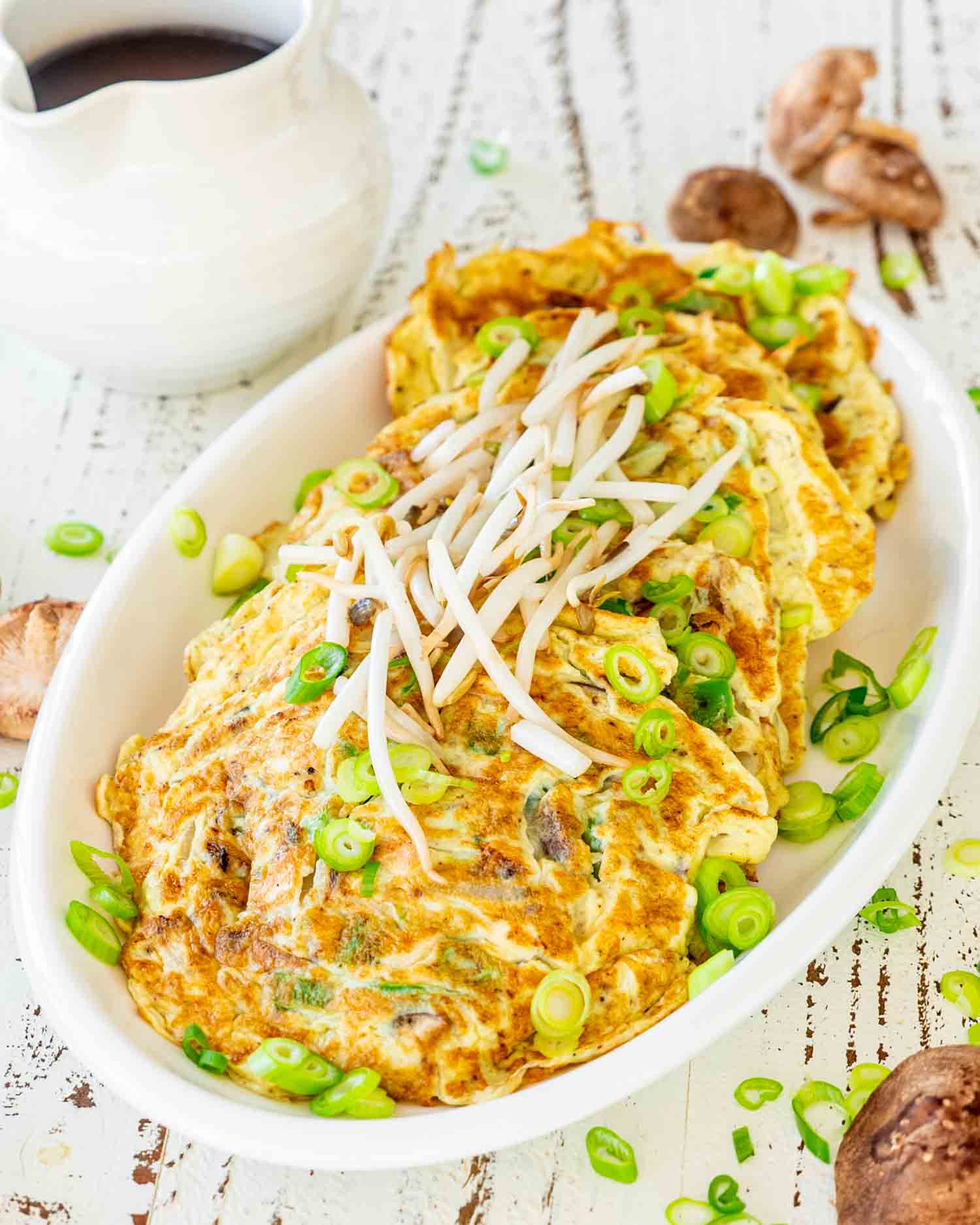 pieces of egg foo young on a white platter topped with bean sprouts.