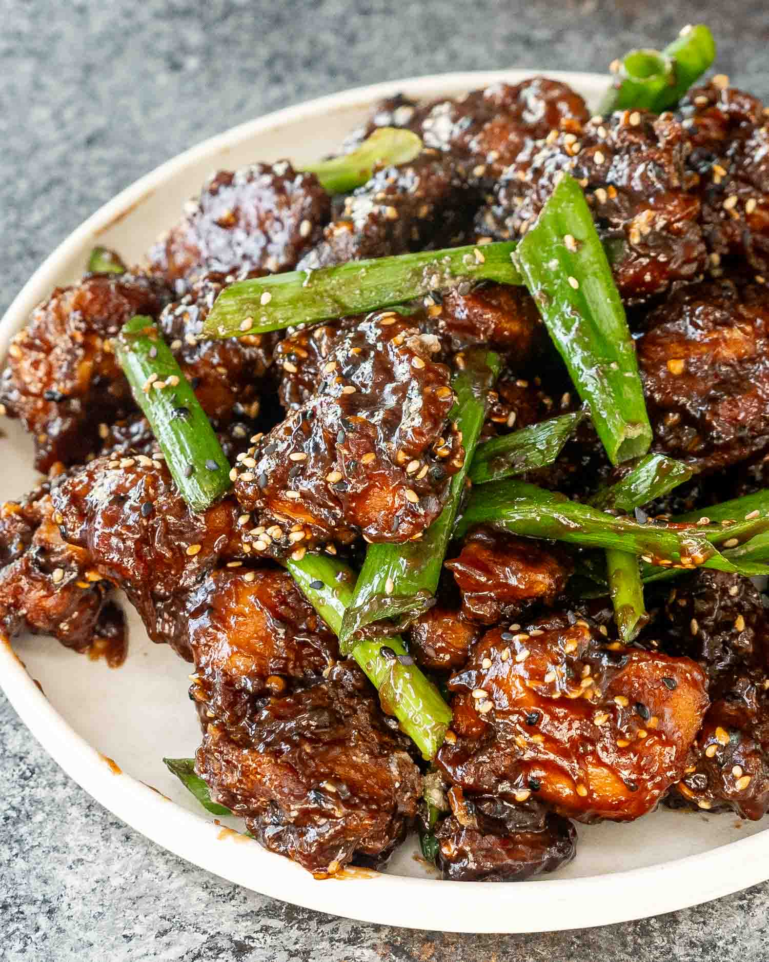 freshly made general tso's chicken garnished with green onions and sesame seeds in a white plate.