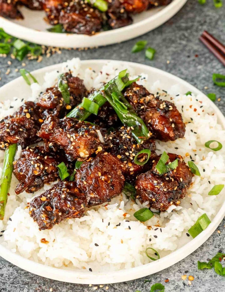 freshly made general tso's chicken garnished with green onions and sesame seeds over a rice in a white plate.