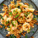 crispy honey walnut shrimp on a metal plate garnished with green onions.