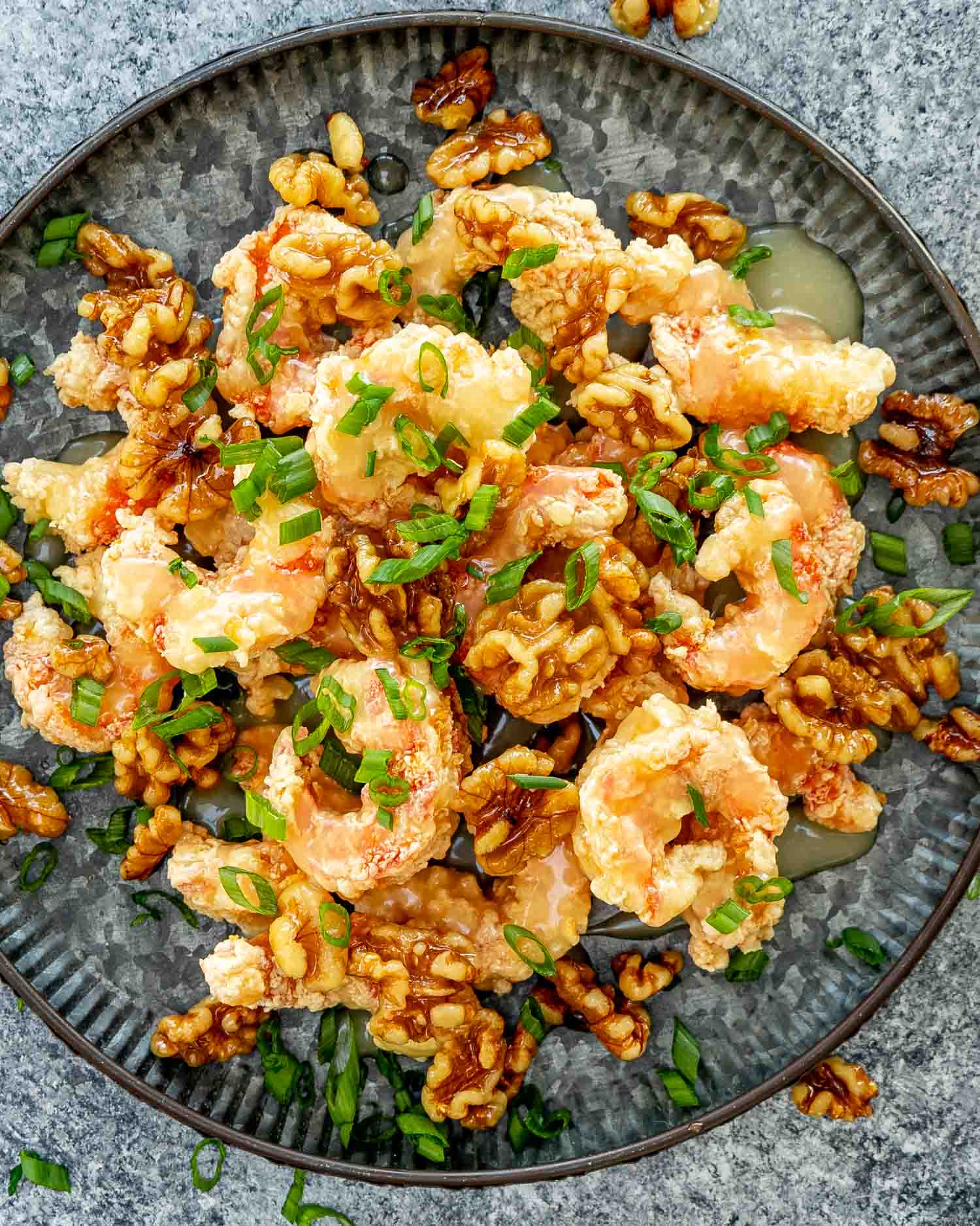crispy honey walnut shrimp on a metal plate garnished with green onions.