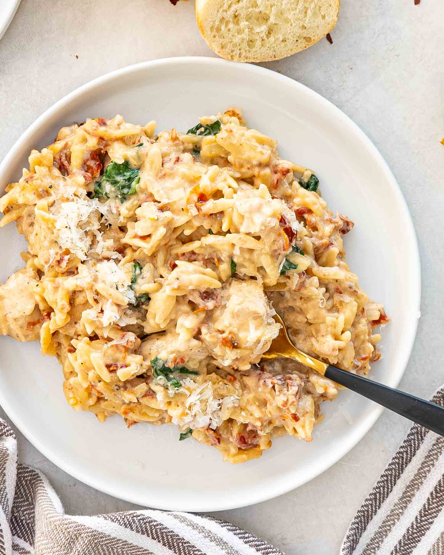a serving of slow cooker creamy tuscan chicken orzo in a white dish with a fork.
