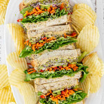 veggie and hummus sandwiches on a white platter along some potato chips.