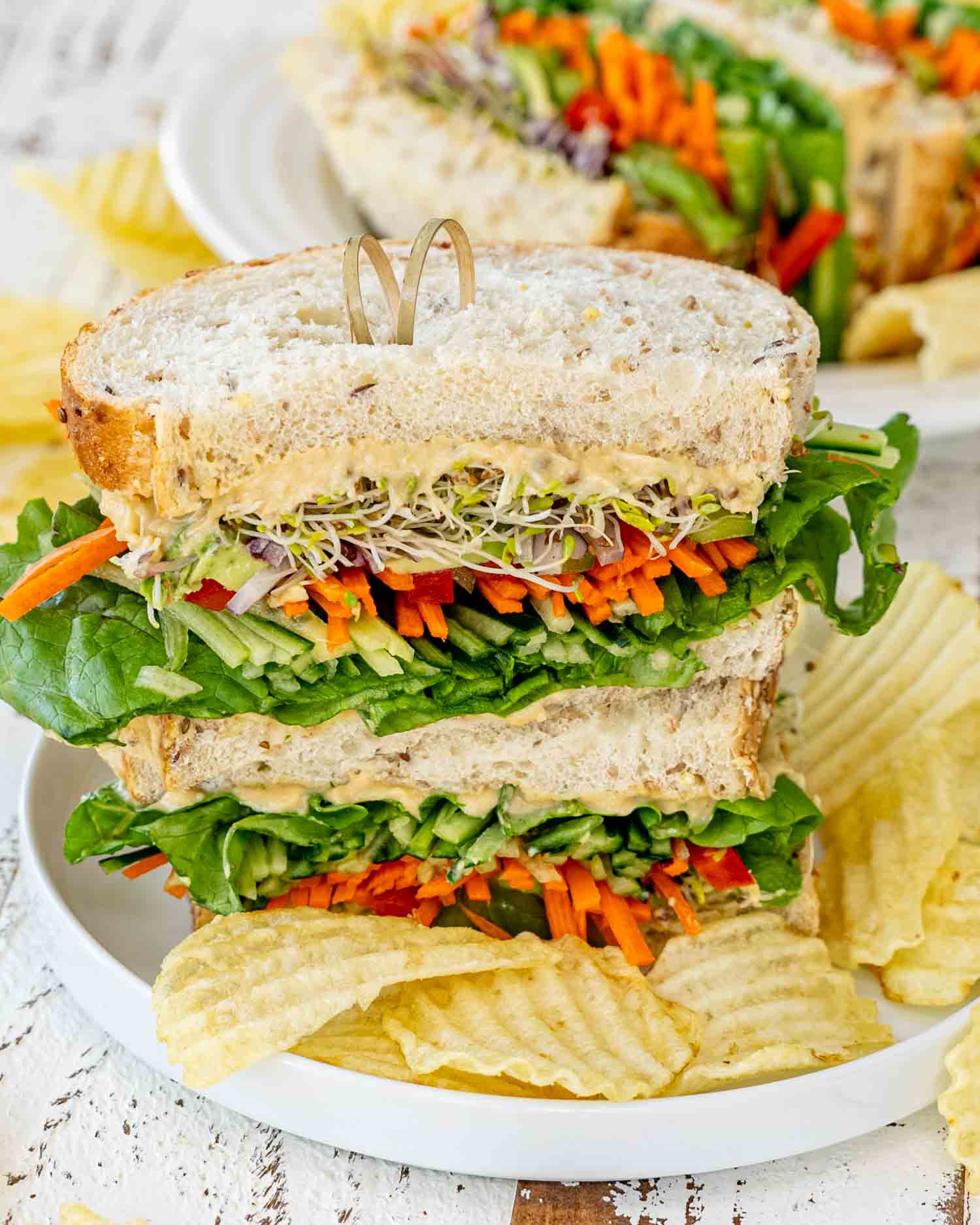 a stack of veggie and hummus sandwich on a plate along some potato chips.