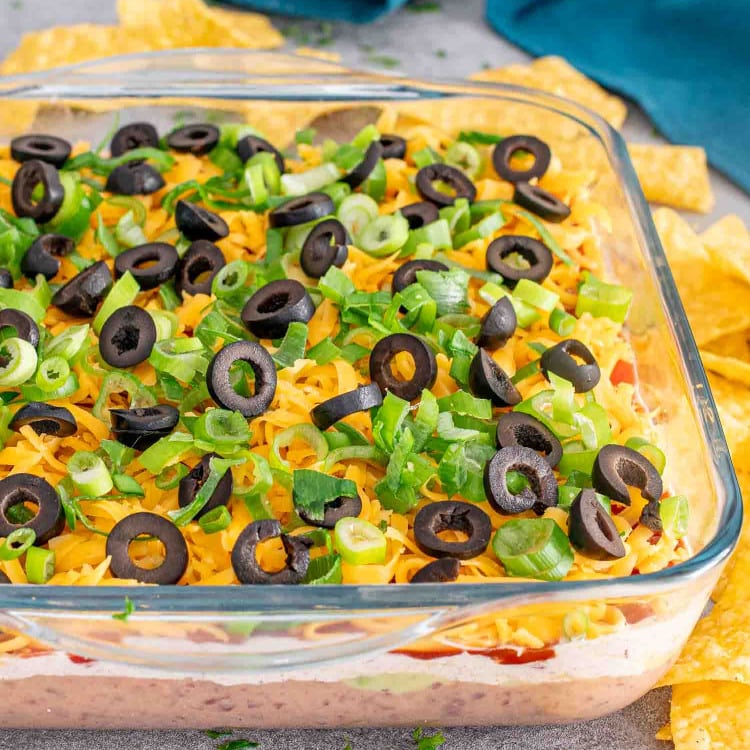 7 layer dip in a square glass dish with some tortilla chips.