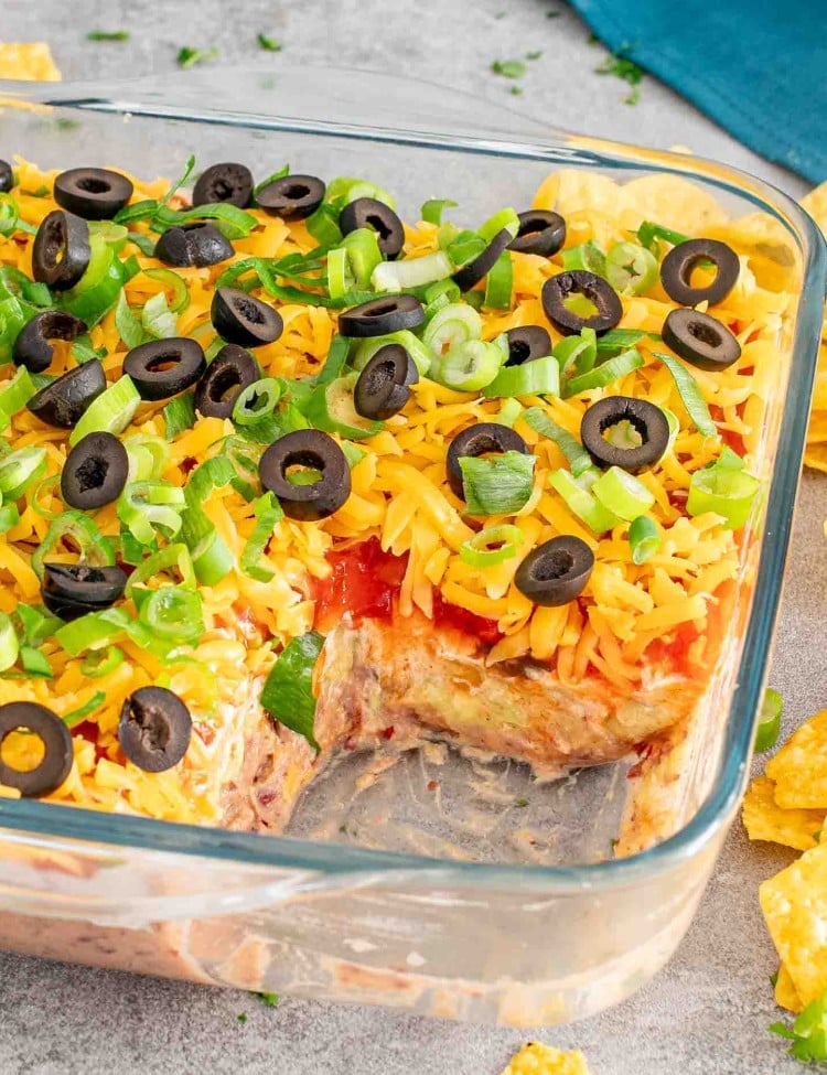 7 layer dip in a square glass dish with some tortilla chips.