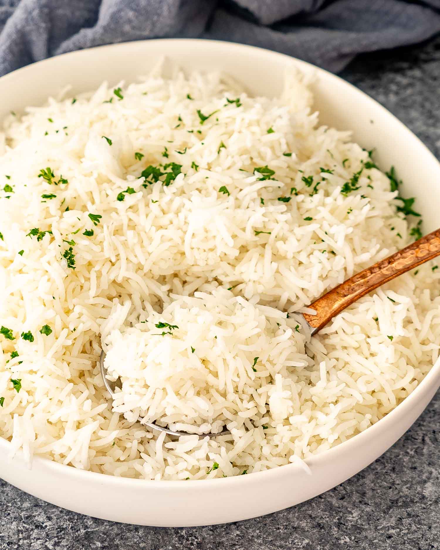 freshly cooked basmati rice in a white bowl garnished with some fresh parsley.