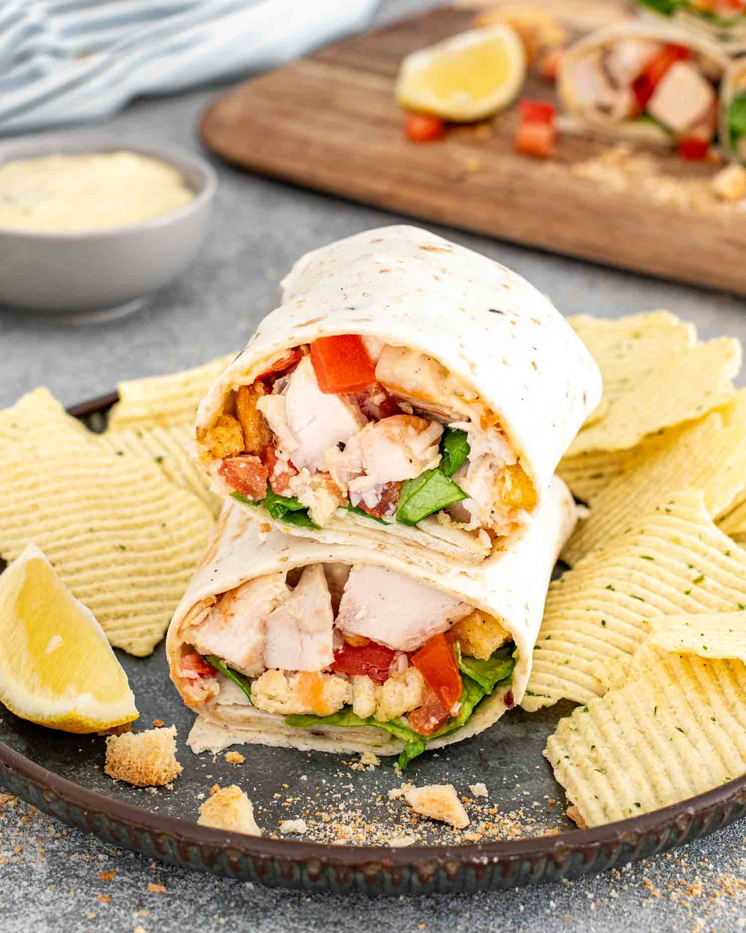 a chicken caesar wrap cut in two on a plate with chips.