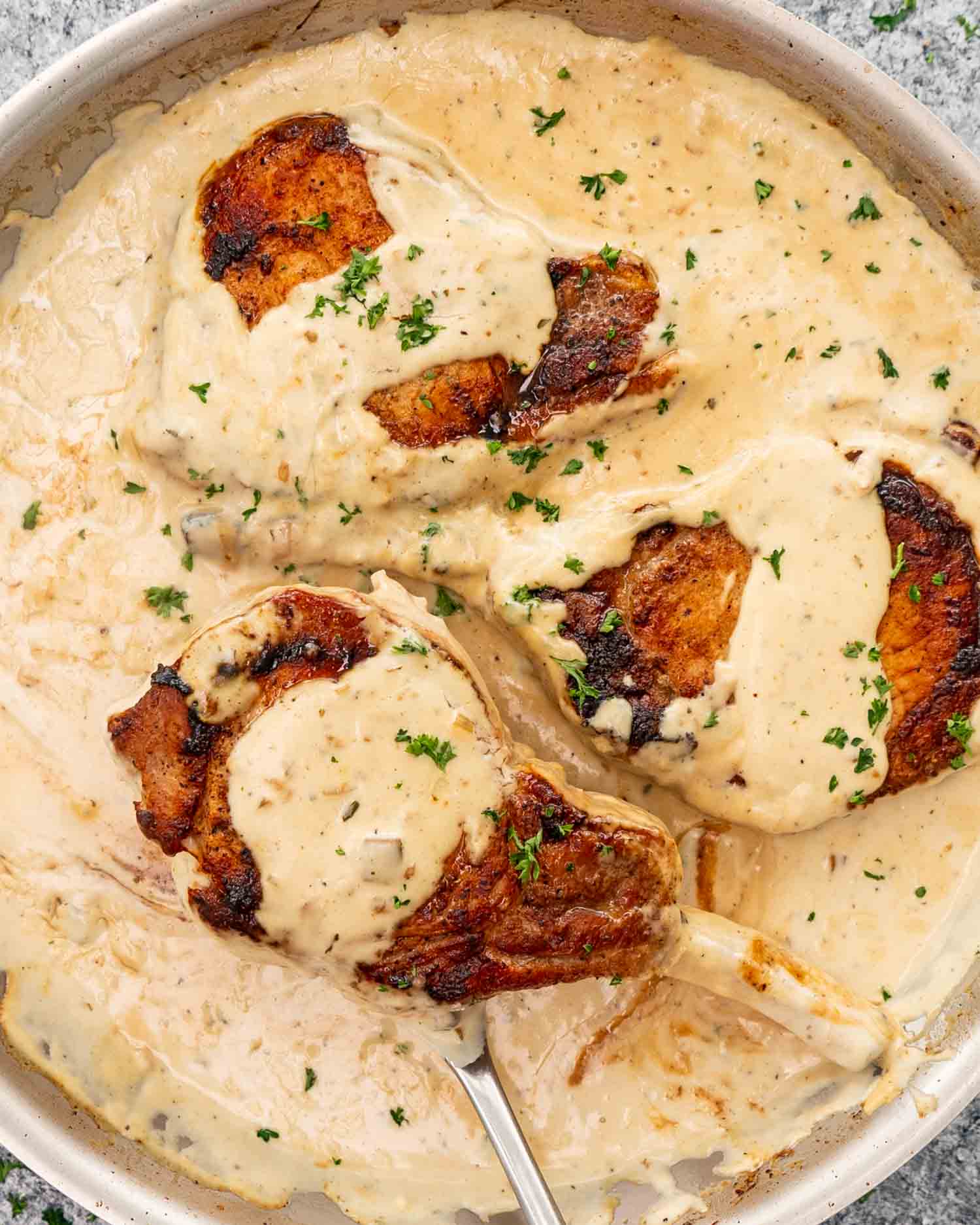 freshly made creamy ranch pork chops in a skillet garnished with parsley.
