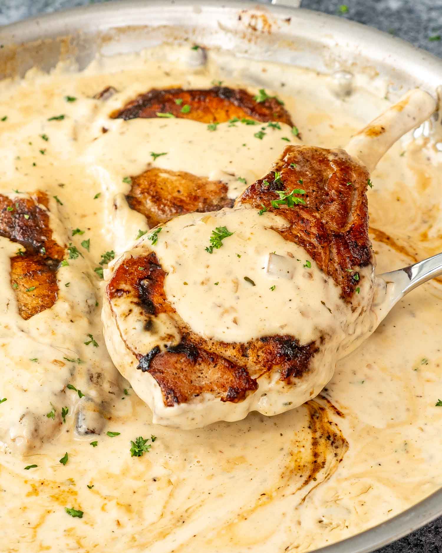 freshly made creamy ranch pork chops in a skillet garnished with parsley.