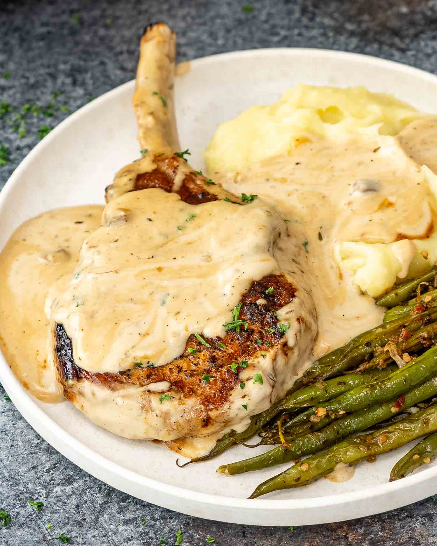 a creamy ranch pork chop along some mashed potatoes and skillet green beans on a plate.