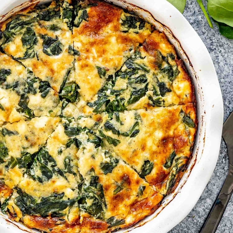 A golden brown, crustless spinach quiche in a white dish, with visible layers of cheese and spinach.