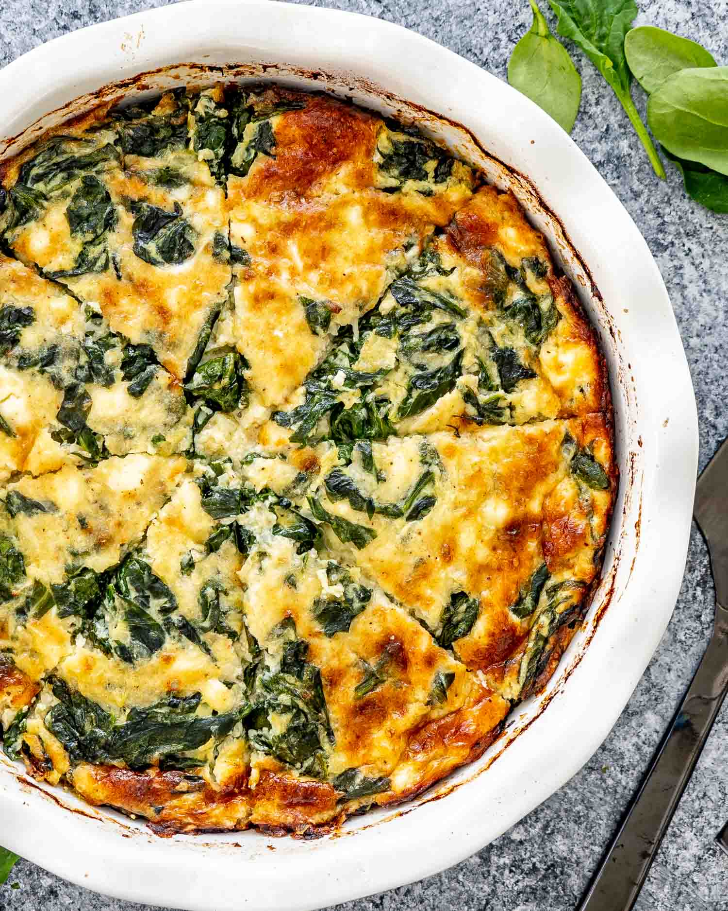 A golden brown, crustless spinach quiche in a white dish, with visible layers of cheese and spinach.