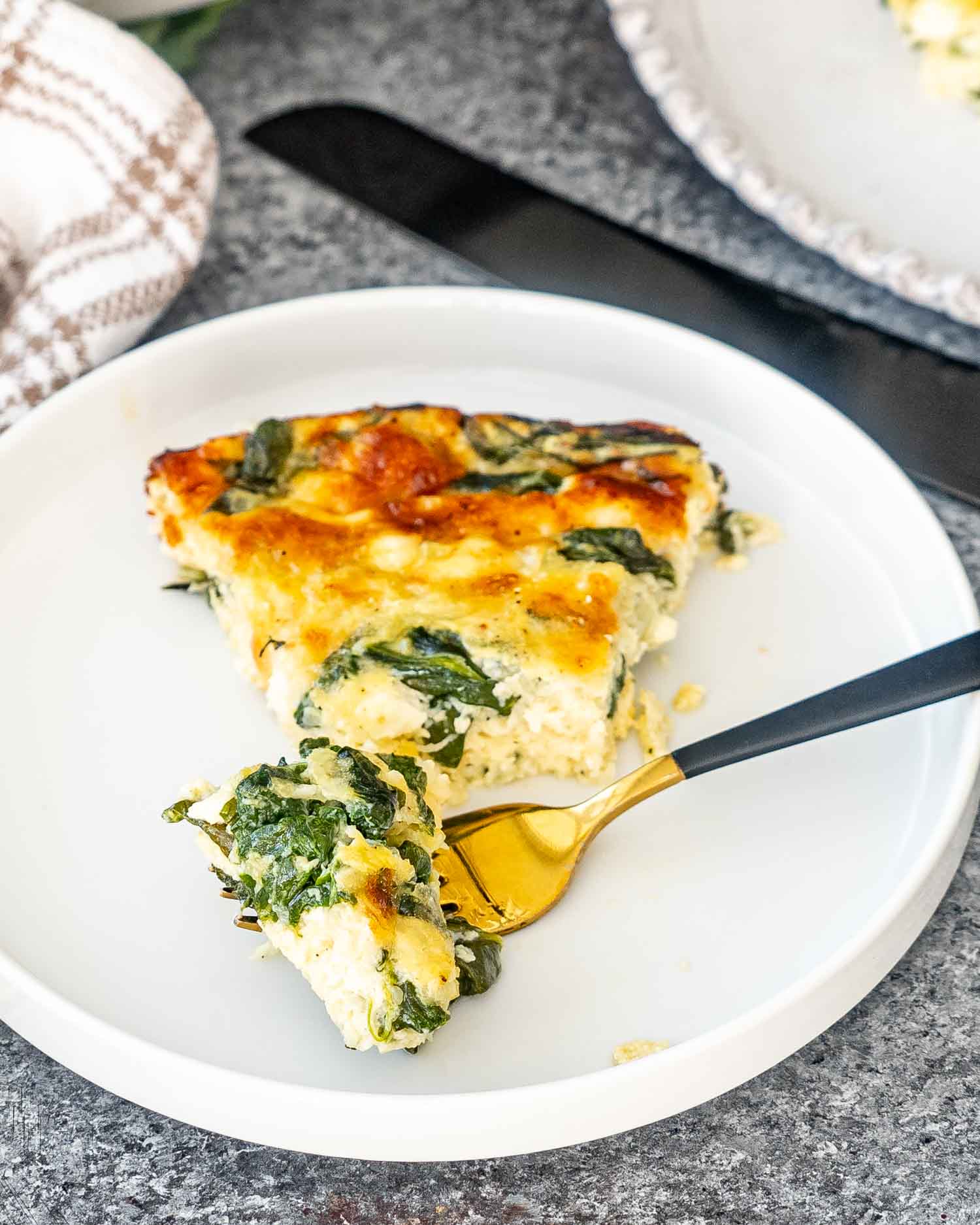 a slice of crustless spinach quiche on a white plate.