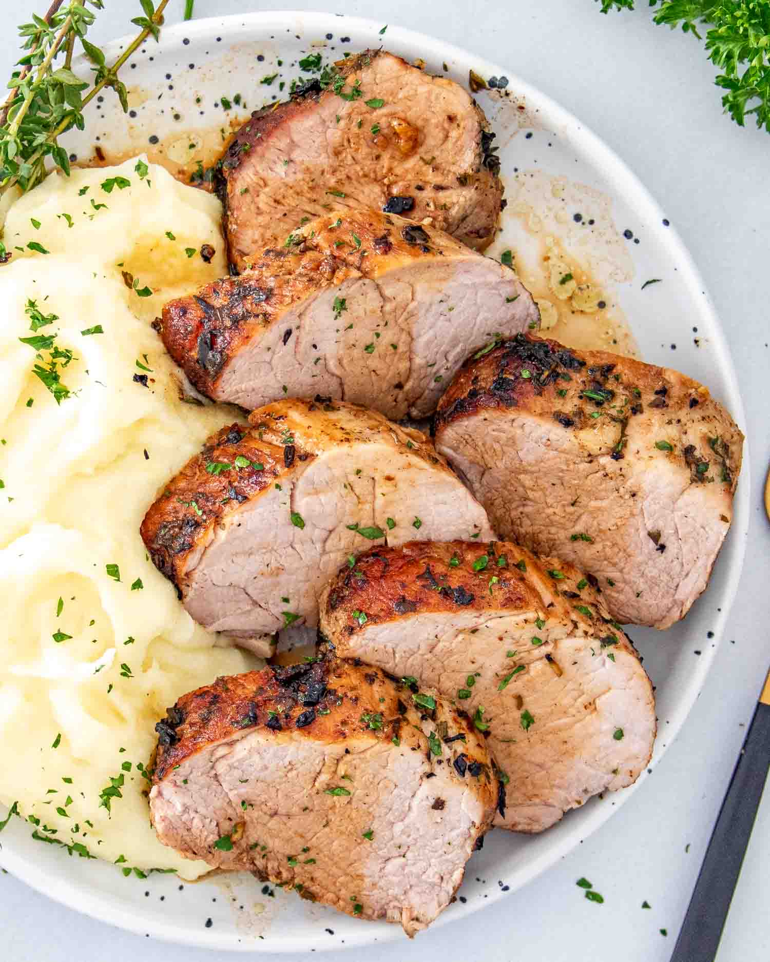 slices of herb crusted pork tenderloin along some mashed potatoes on a white plate.