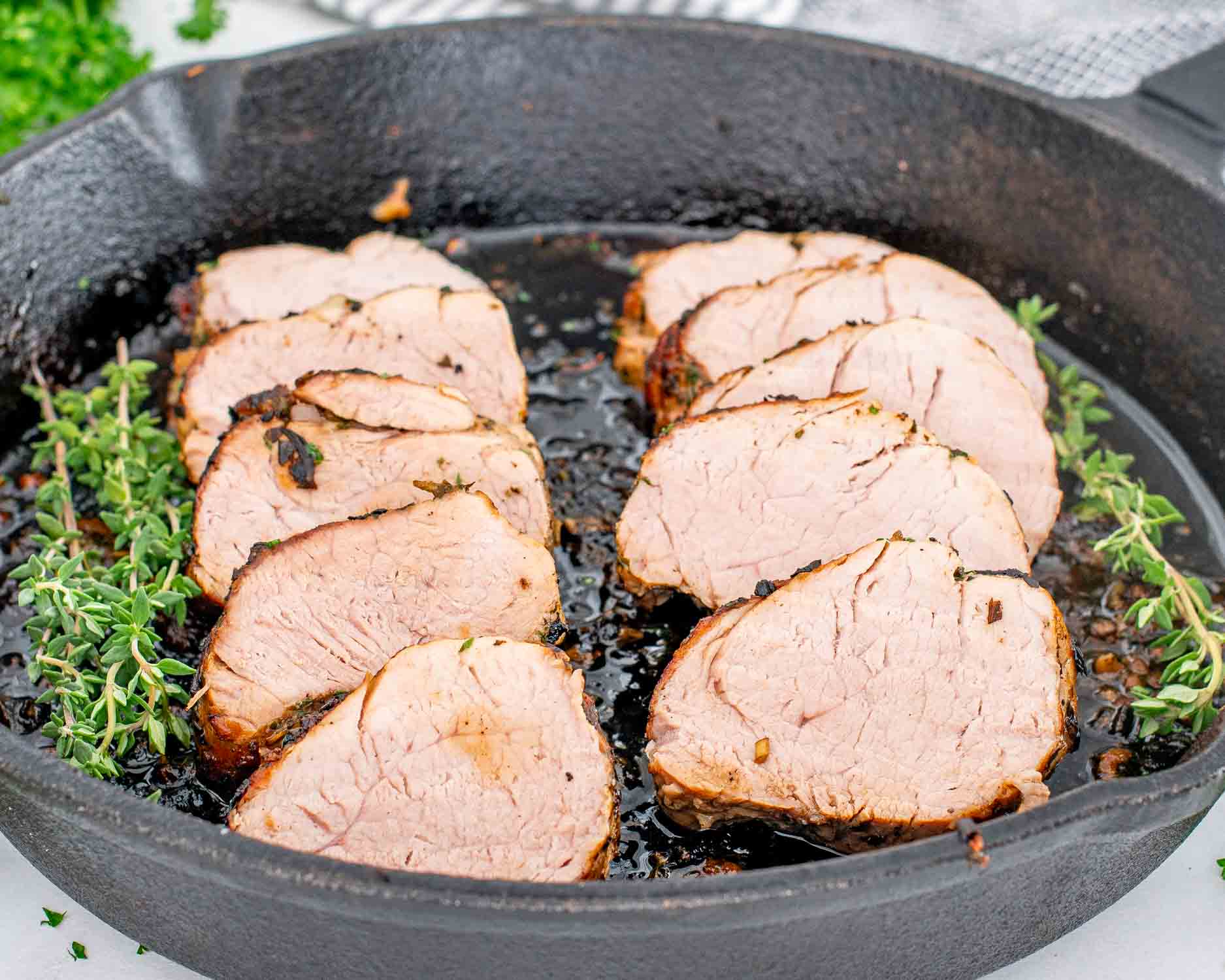 a cast iron skillet with sliced herb crusted pork tenderloin.