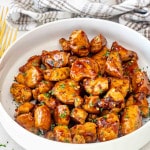 sticky, sweet and garlicky honey chicken bites in a white bowl.