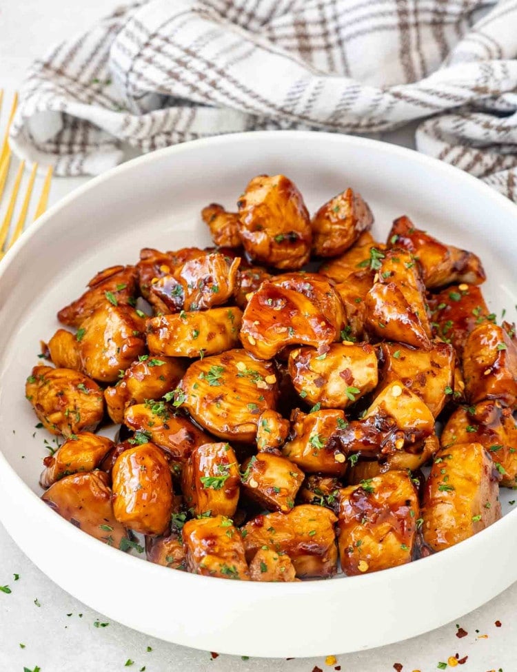 sticky, sweet and garlicky honey chicken bites in a white bowl.
