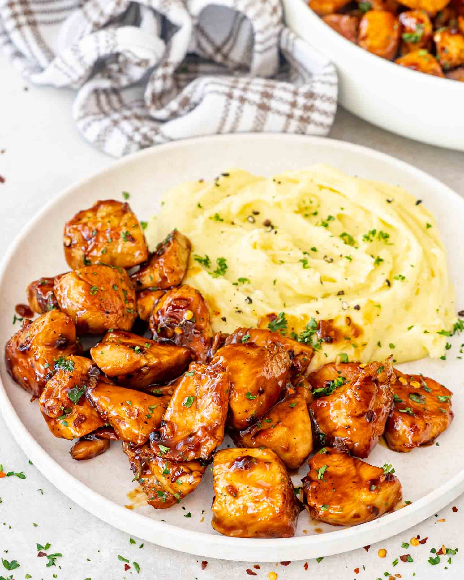 a serving of honey garlic chicken bites with some mashed potatoes on a white plate.