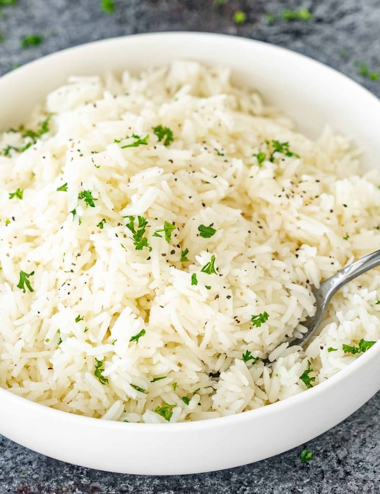 a white bowl with perfectly cooked jasmine rice garnished with some parsley.