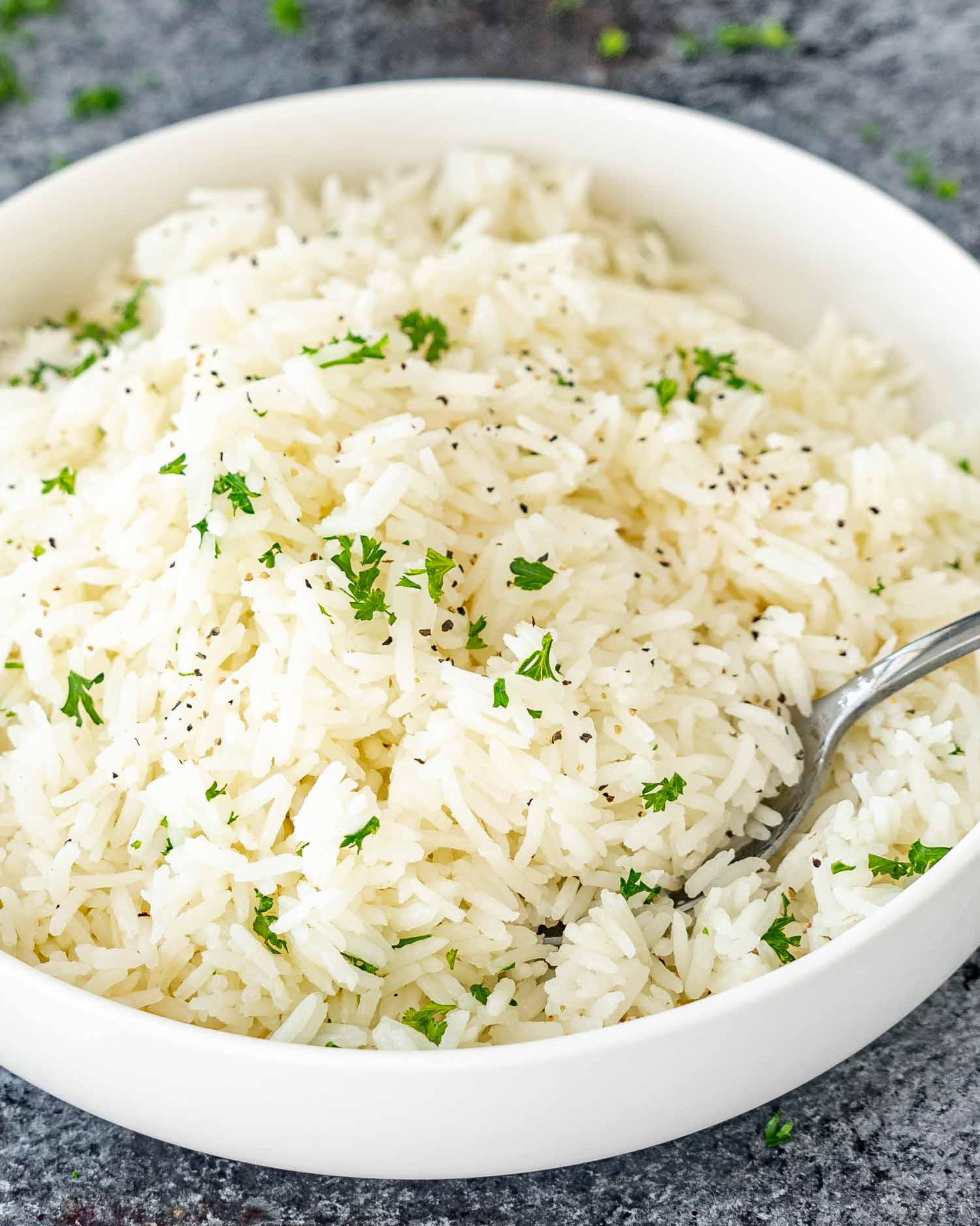 a white bowl with perfectly cooked jasmine rice garnished with some parsley.