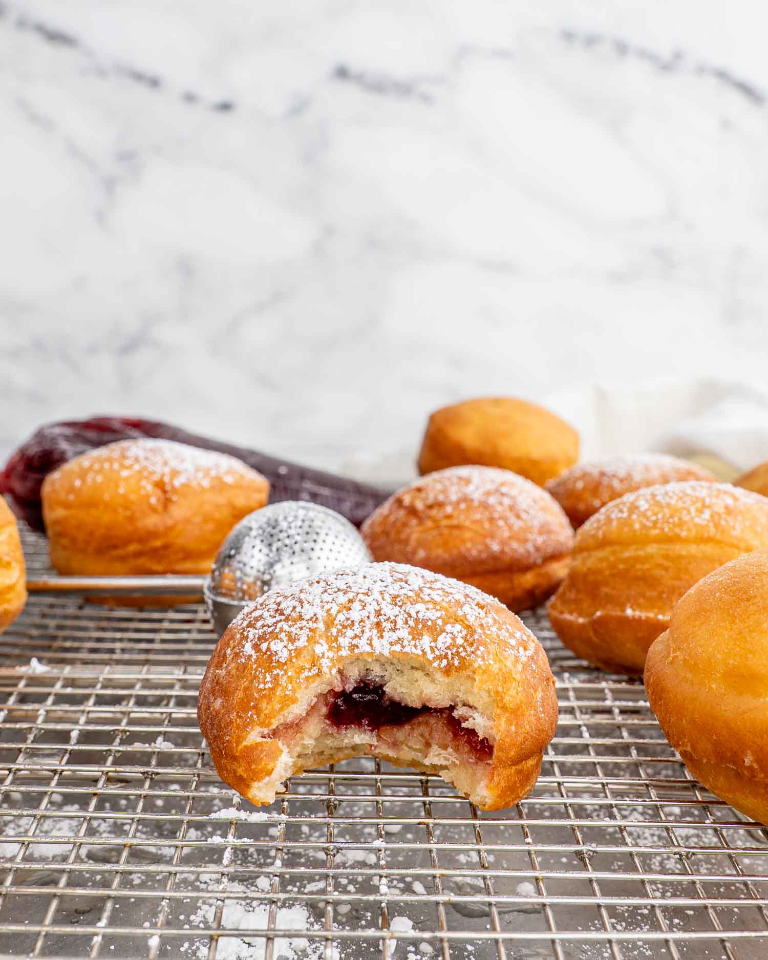 jelly donuts filled with cherry jelly on a cooling rack over a baking sheet.
