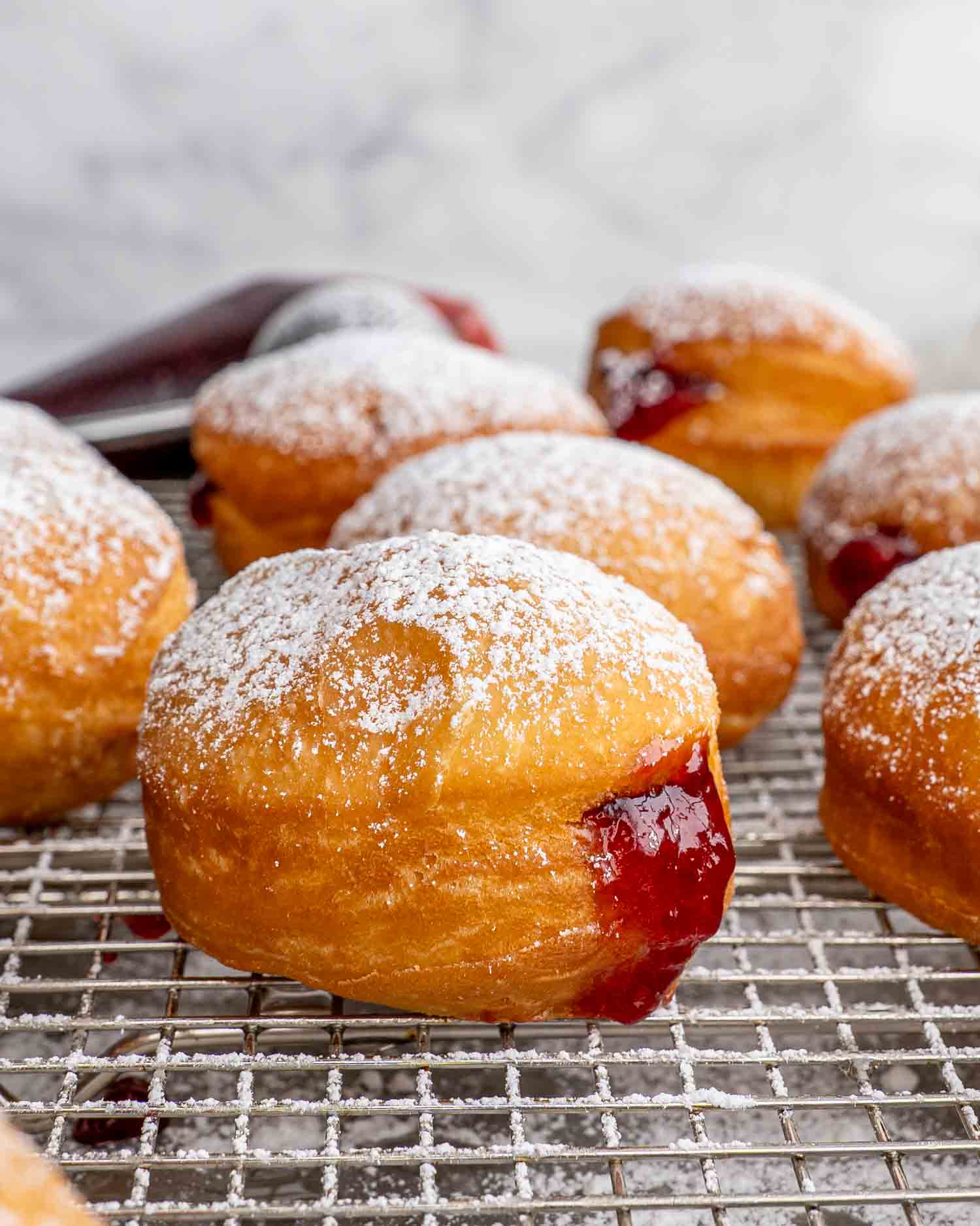 jelly donuts filled with cherry jelly on a cooling rack over a baking sheet.