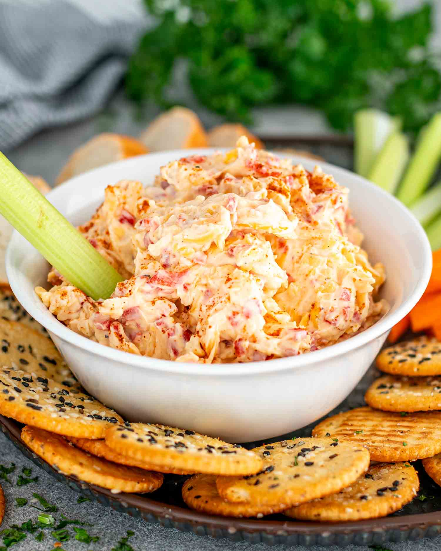 pimento cheese in a white bowl along some crackers, celery and carrot sticks.