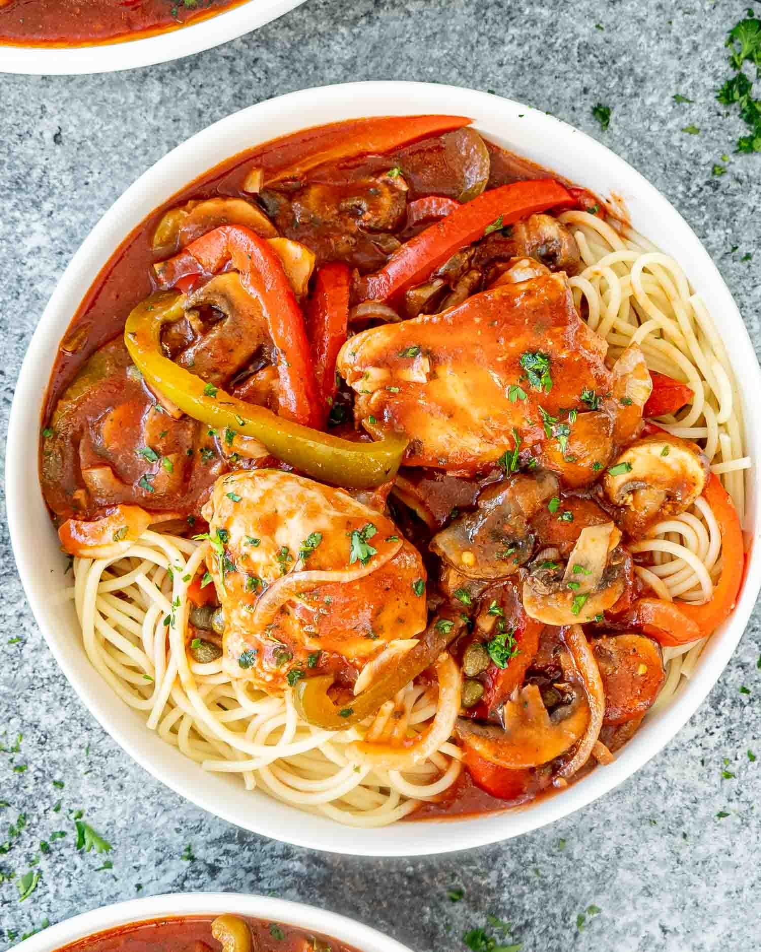 a serving of chicken cacciatore that was made in the slow cooker over cooked spaghetti in a white bowl.