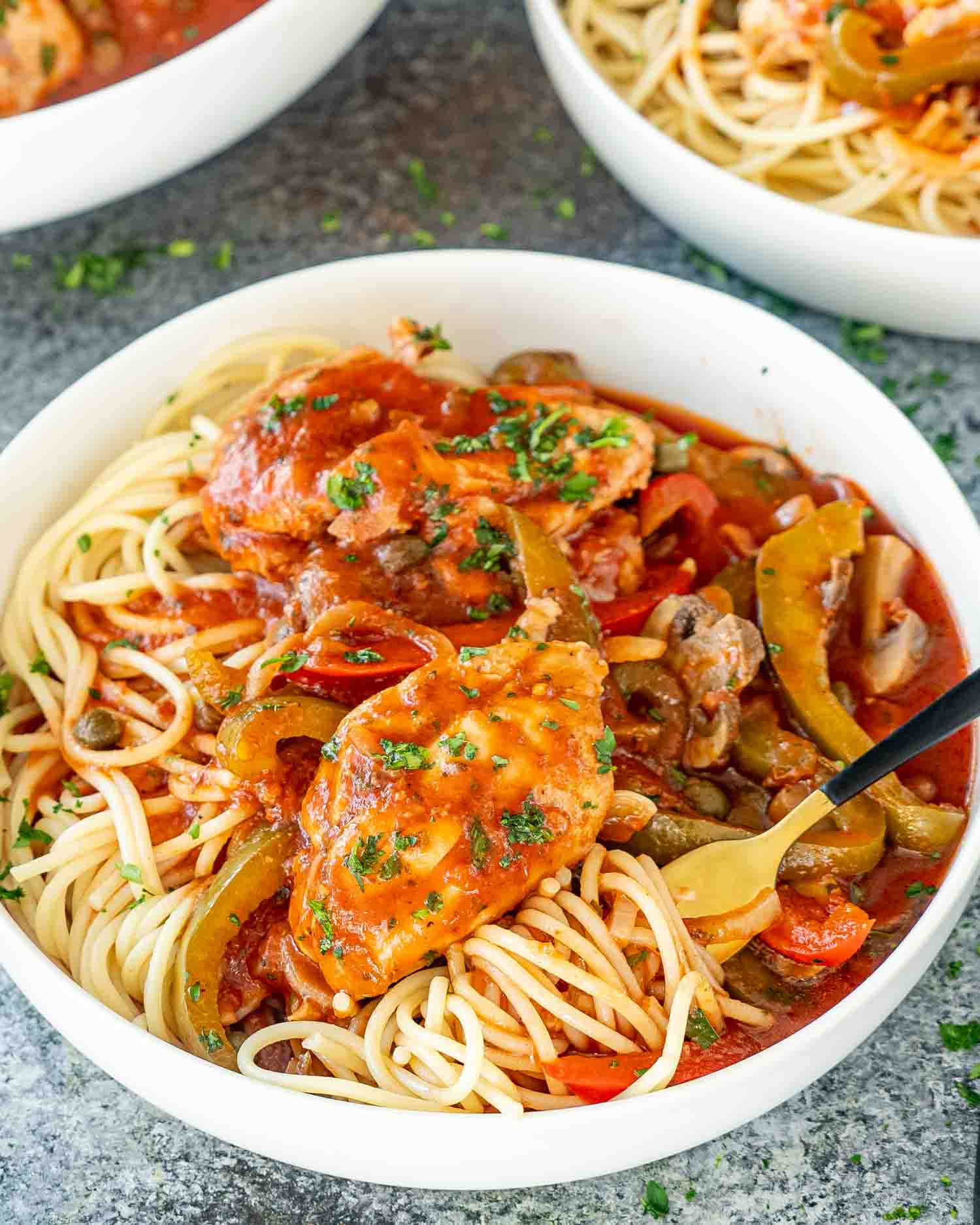 a serving of chicken cacciatore that was made in the slow cooker over cooked spaghetti in a white bowl.