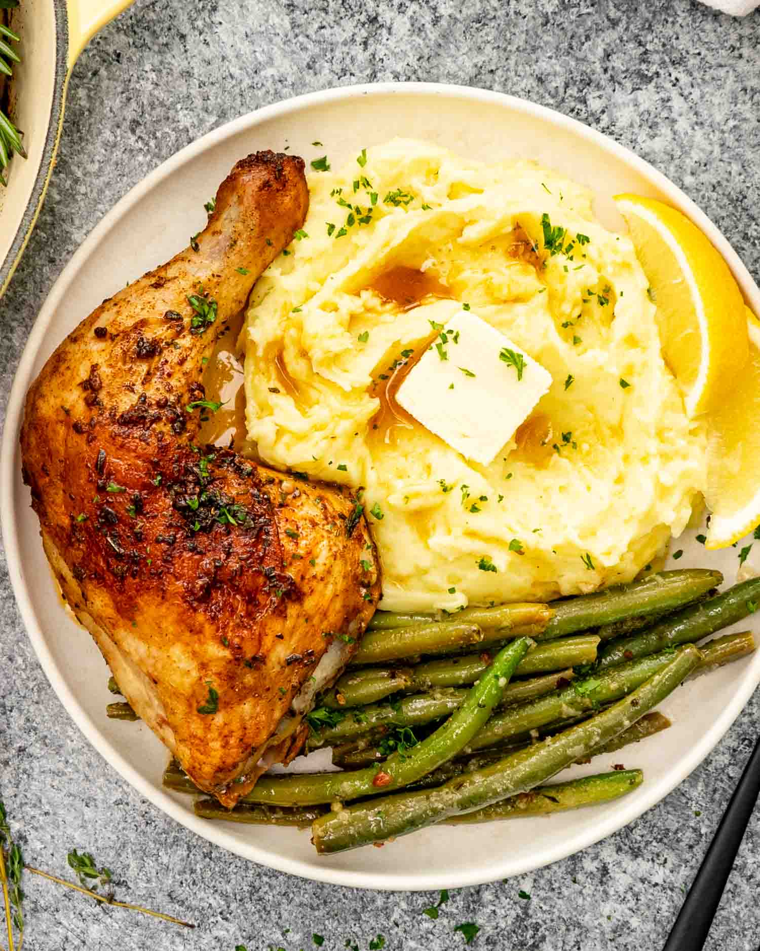 a baked chicken leg on a white plate with a side of mashed potatoes and green beans.