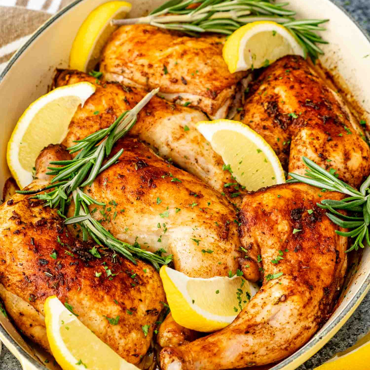 fresh out of the oven baked chicken legs in a baking pan garnished with lemon wedges and rosemary.