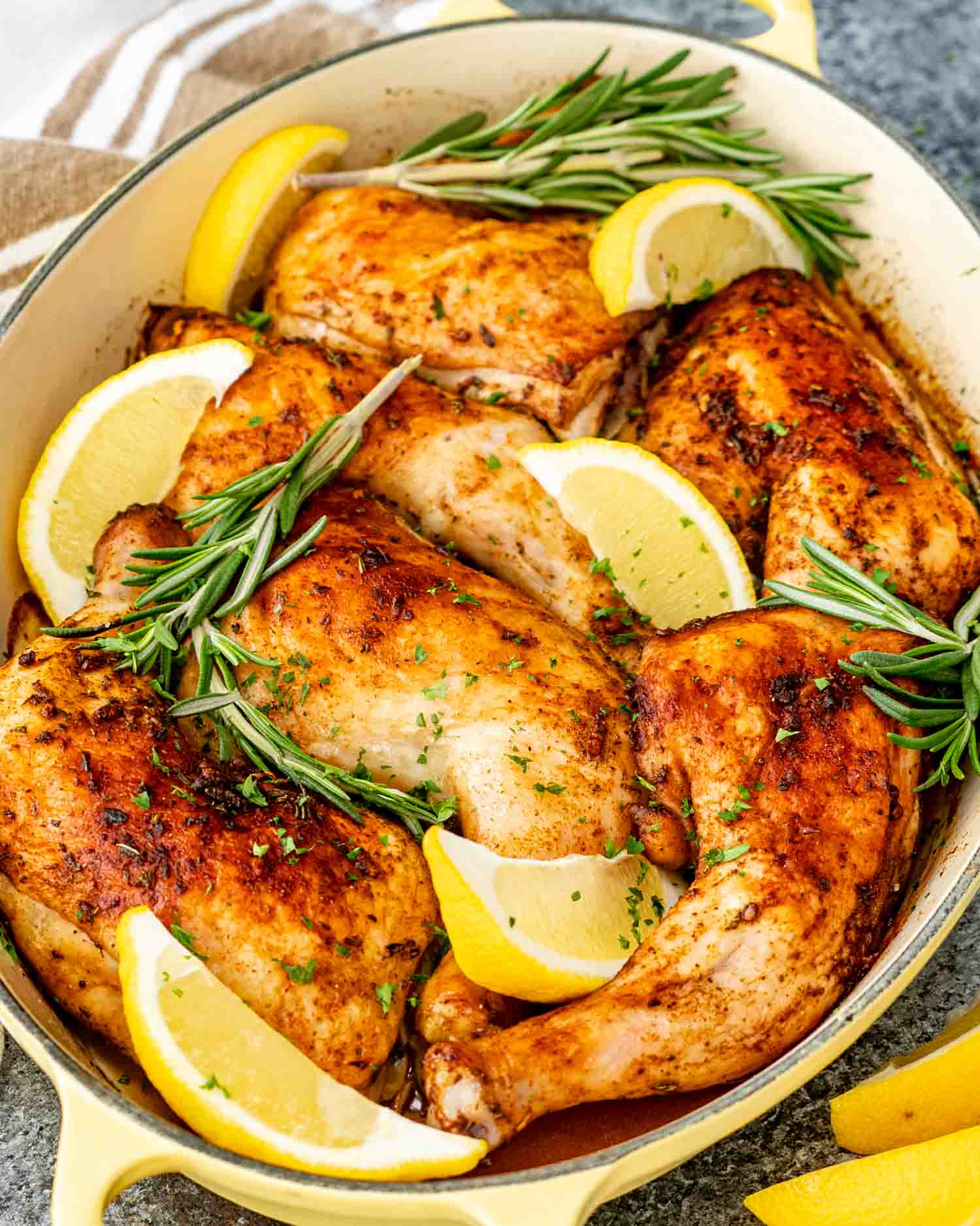 fresh out of the oven baked chicken legs in a baking pan garnished with lemon wedges and rosemary.