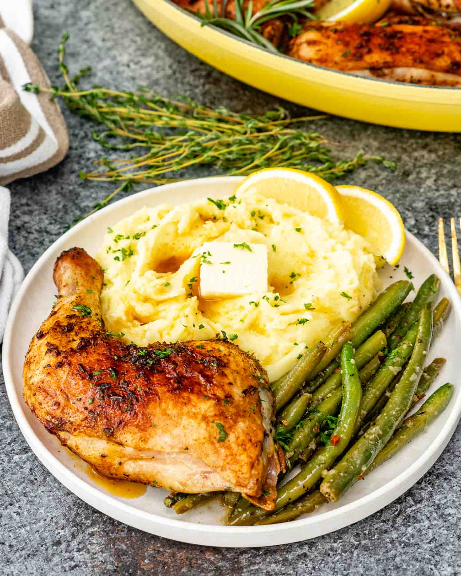 a baked chicken leg on a white plate with a side of mashed potatoes and green beans.