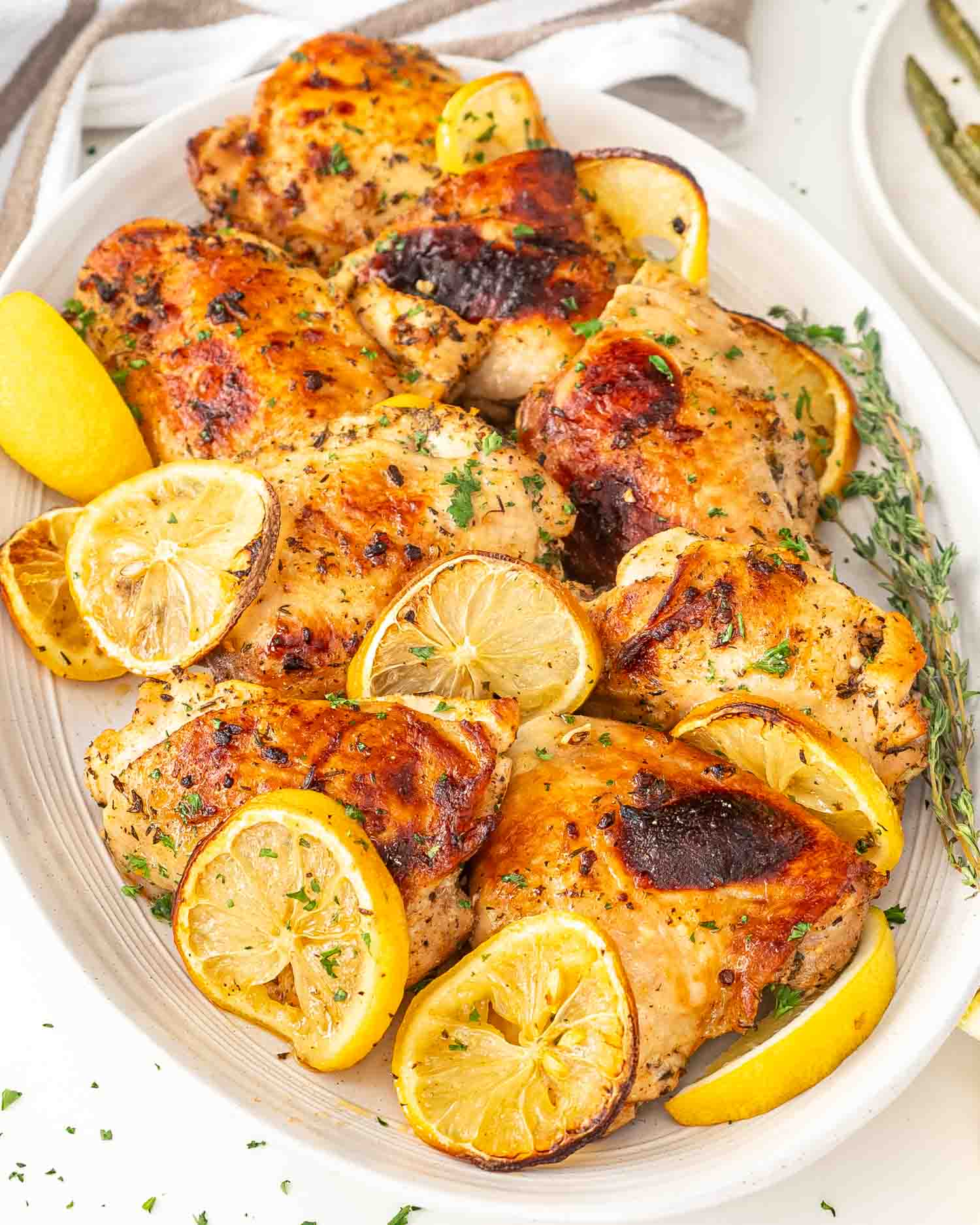 baked lemon chicken thighs on a platter garnished with lemon slices and parlsey.