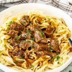 beef and noodles in a white bowl garnished with a bit of parsley.