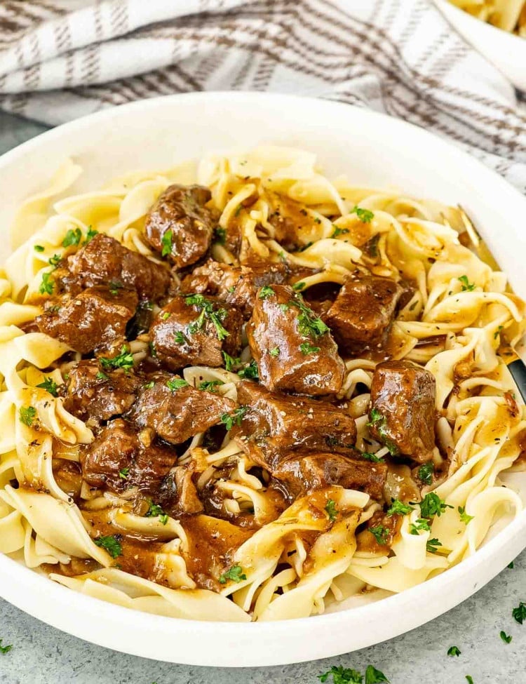 beef and noodles in a white bowl garnished with a bit of parsley.