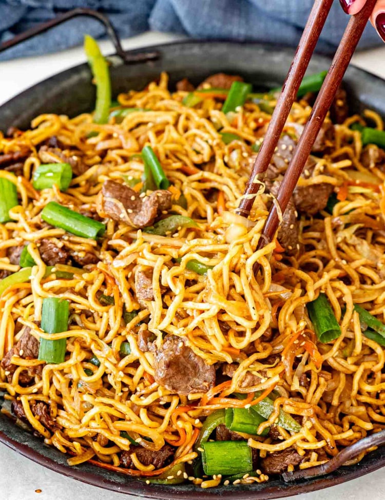 fresh beef chow mein garnished with green onions in a metal plate.