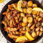 chicken and potato skillet garnished with lemon wedges, parsley and red pepper flakes.