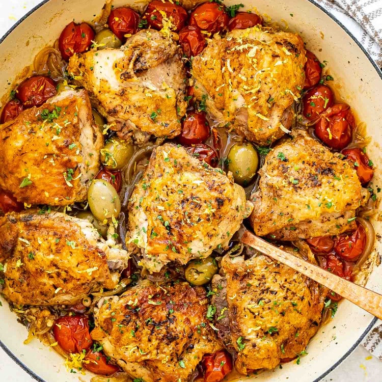 chicken provencal in a dutch oven garnished with parsley and lemon zest.