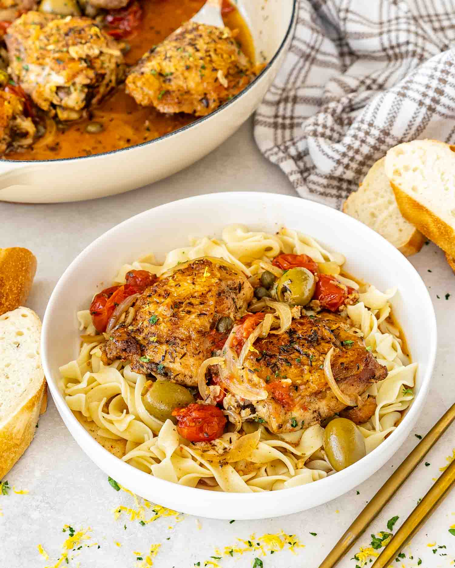 chicken provencal on a bed of noodles in a white bowl.