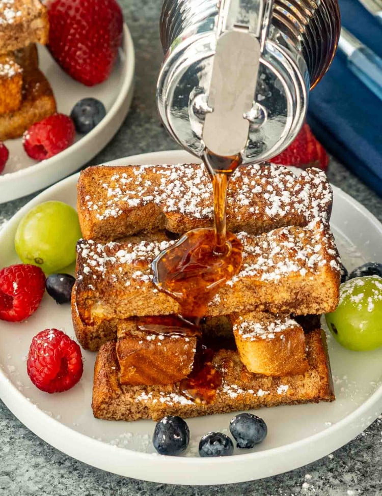 a hand drizzling maple syrup on a stack of air fryer french toast sticks.