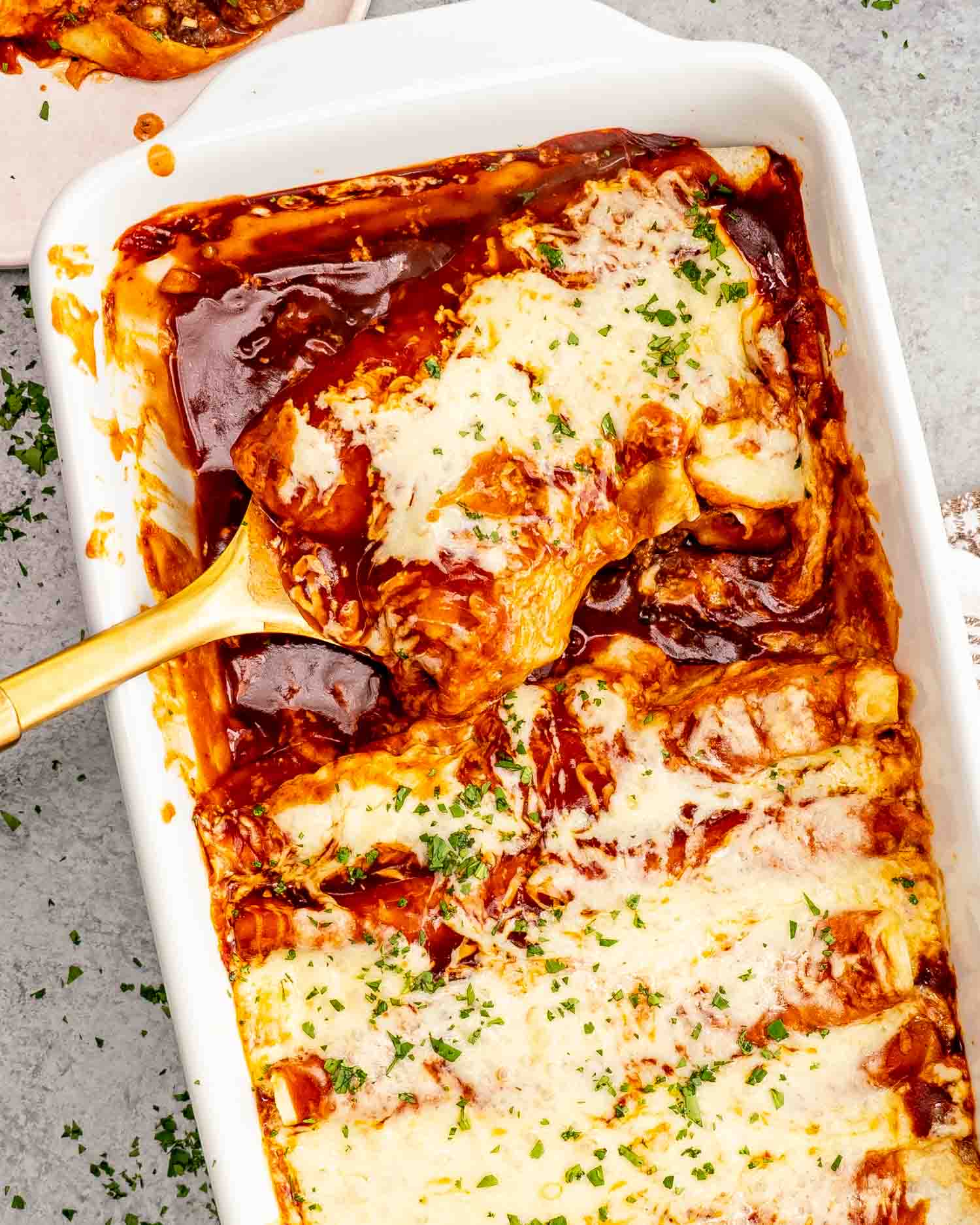freshly baked cheesy beef enchiladas in a white casserole dish garnished with fresh cilantro.