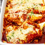freshly baked cheesy beef enchiladas in a white casserole dish garnished with fresh cilantro.