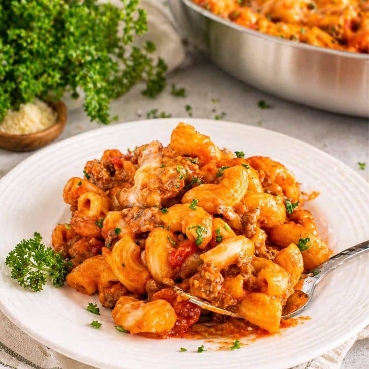 Professional shot of one pot beefaroni with melted cheese and fresh parsley served on a white ribbed plate.
