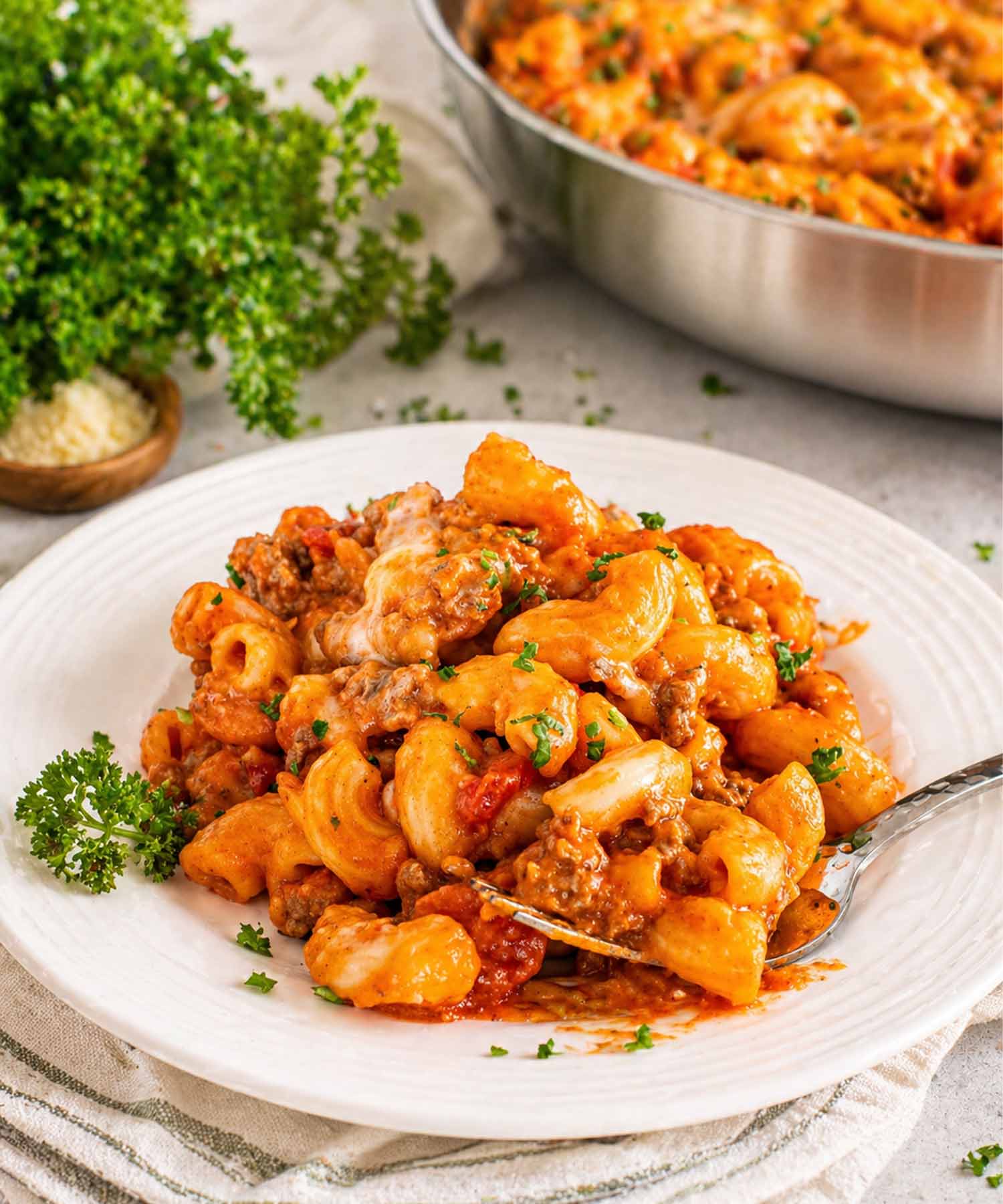 Professional shot of one pot beefaroni with melted cheese and fresh parsley served on a white ribbed plate.