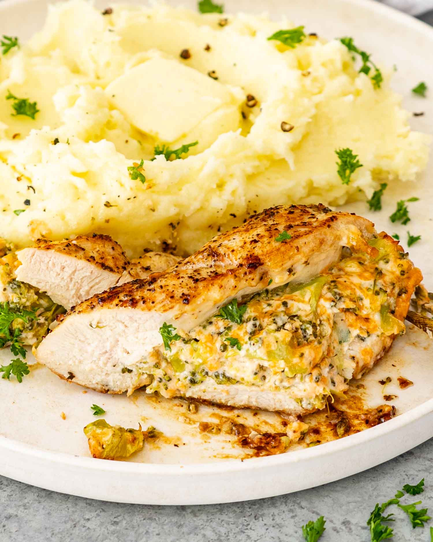 a serving of broccoli and cheddar stuffed chicken breast with mashed potatoes on a white plate.